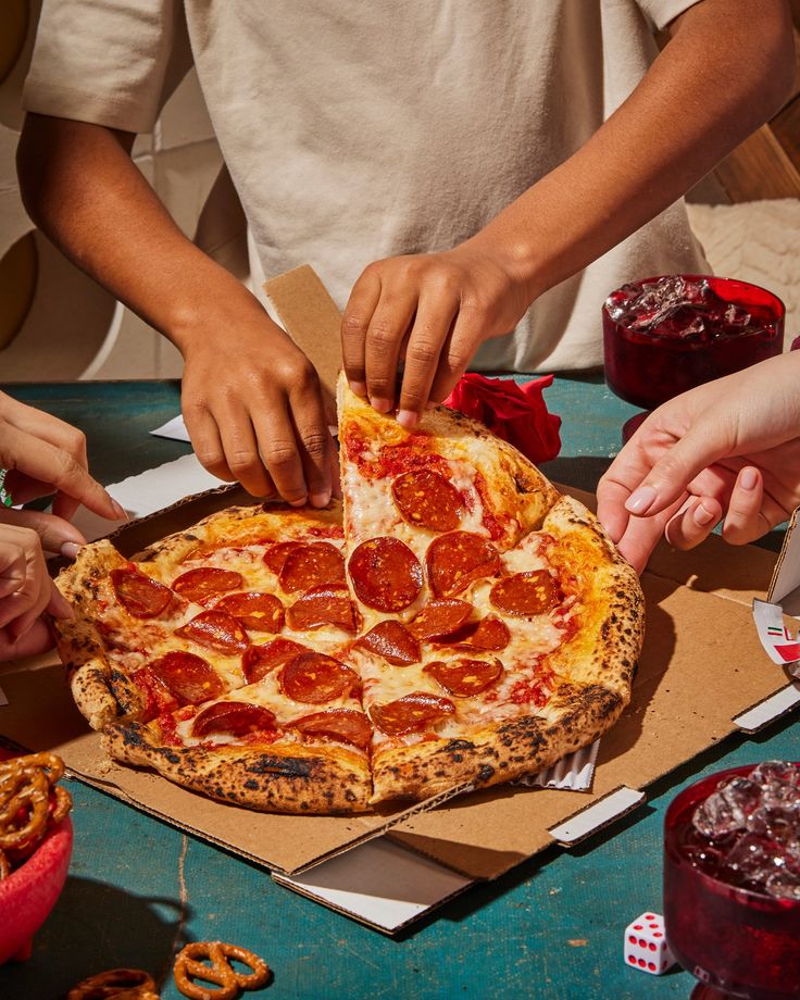 Varias manos tomando rebanadas de una pizza compartida en una reunión