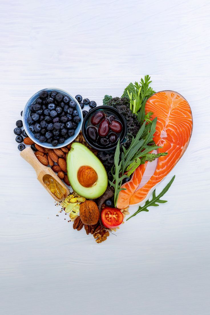 Alimentos saludables para el corazón acomodados en forma de corazón: salmón, aguacate, arándanos y nueces